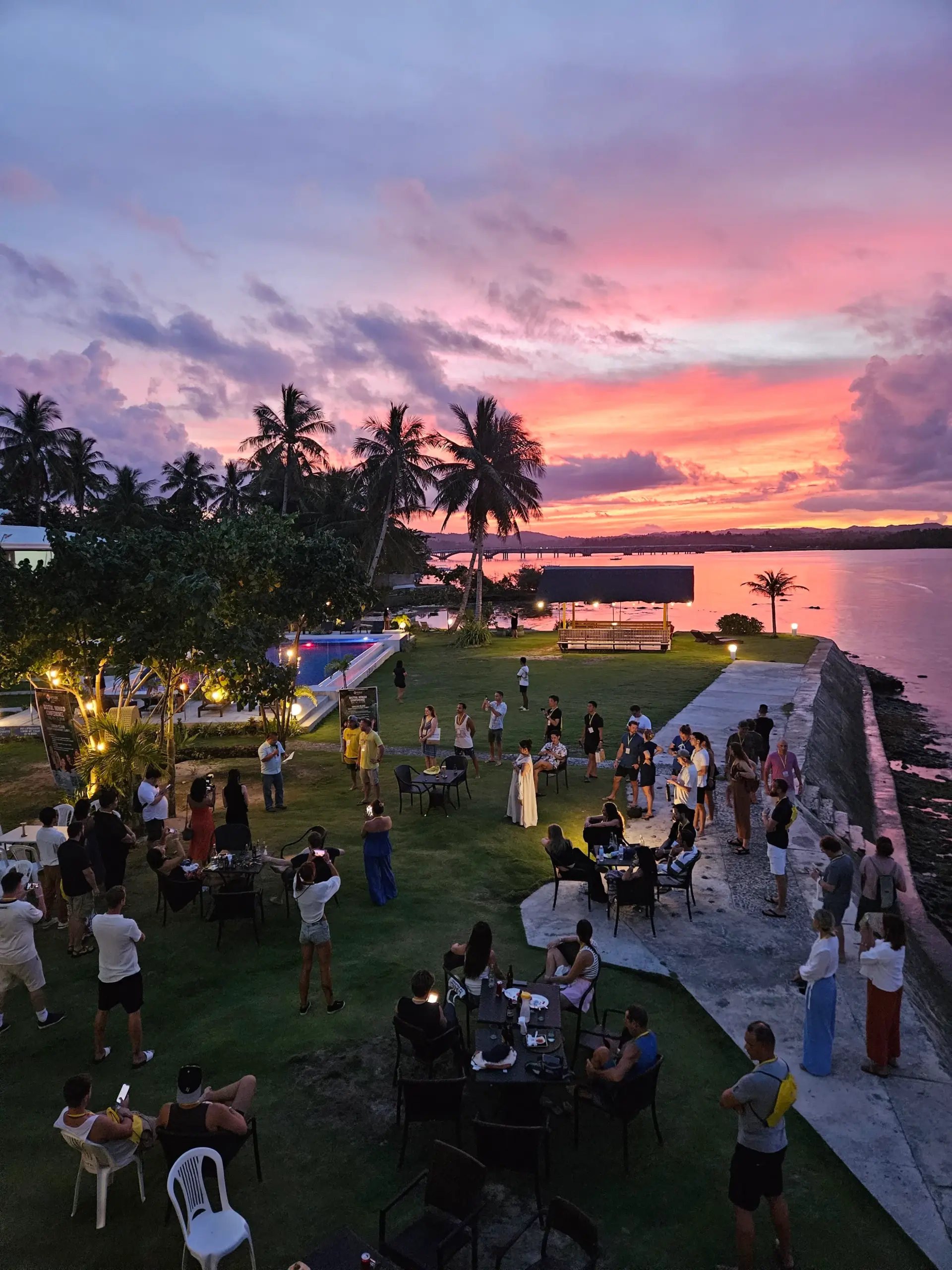 Sunset lawn reception by the water with palm trees and coastal bridge at Nomads in Paradise Siargao