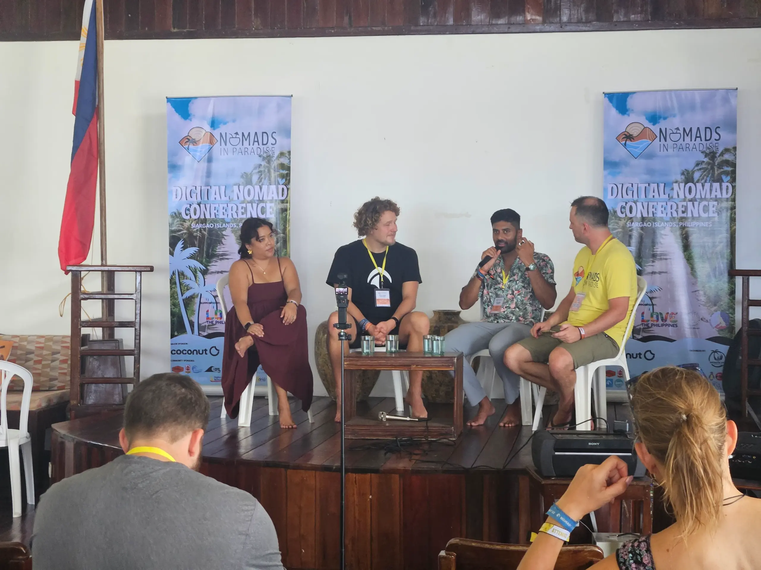 Four barefoot panelists on stage at Nomads in Paradise conference with Philippine flag
