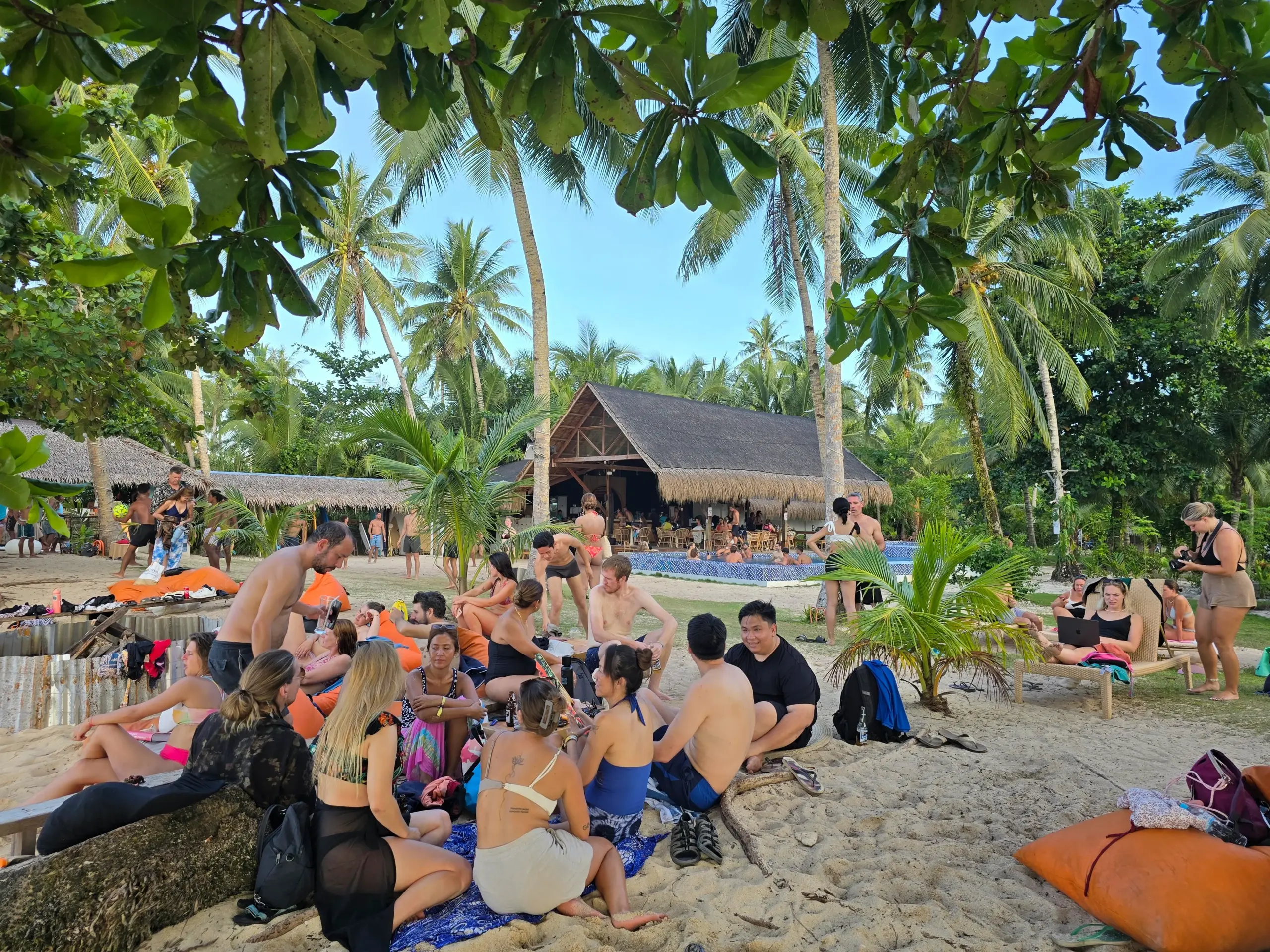 Digital nomads networking in a circle on sandy beach with beanbags and thatched lounge in Siargao