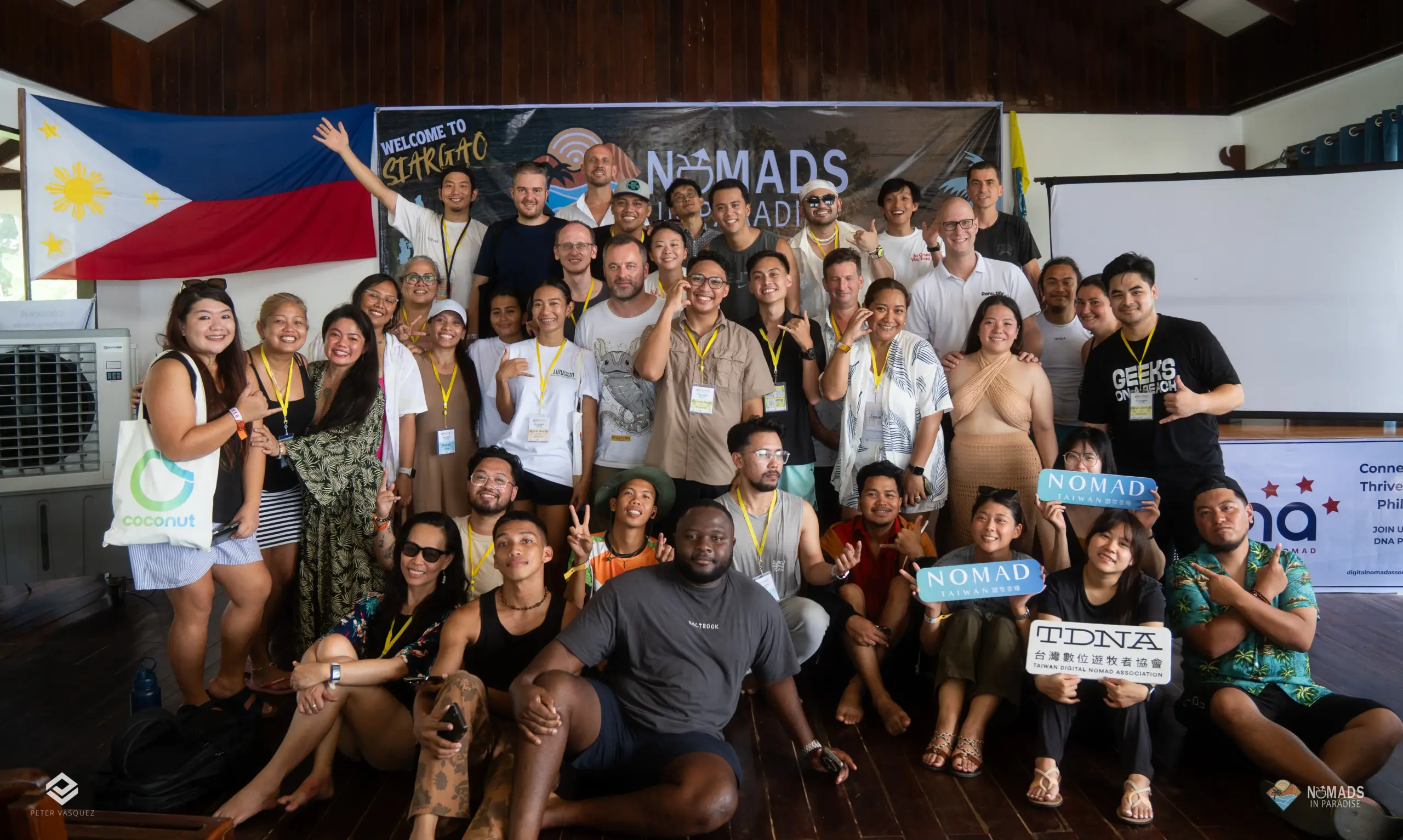 Large diverse group photo inside wooden venue under Nomads in Paradise banner — international community