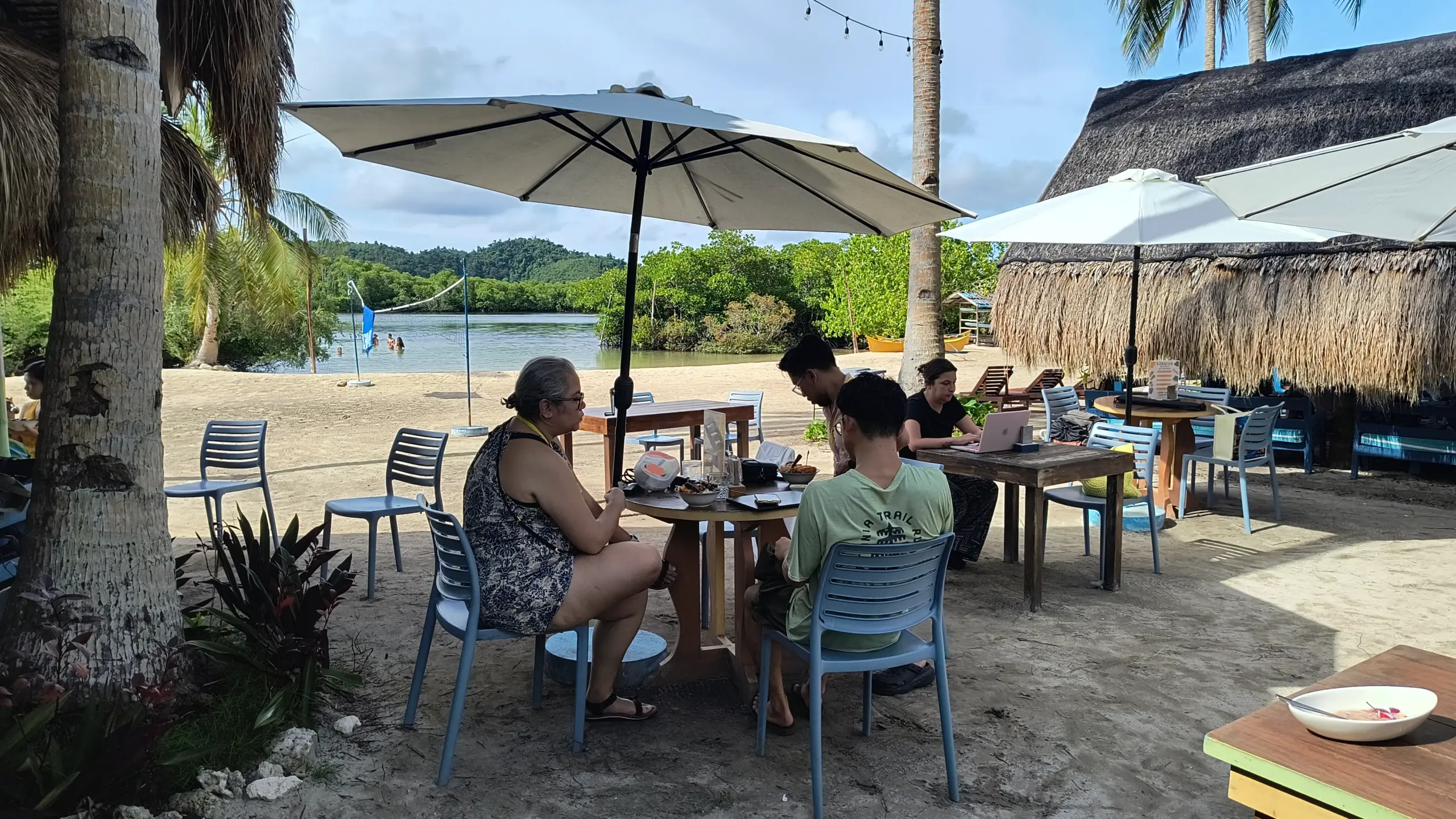 Conference attendees working on laptops beside calm tropical lagoon at Nomads in Paradise Siargao