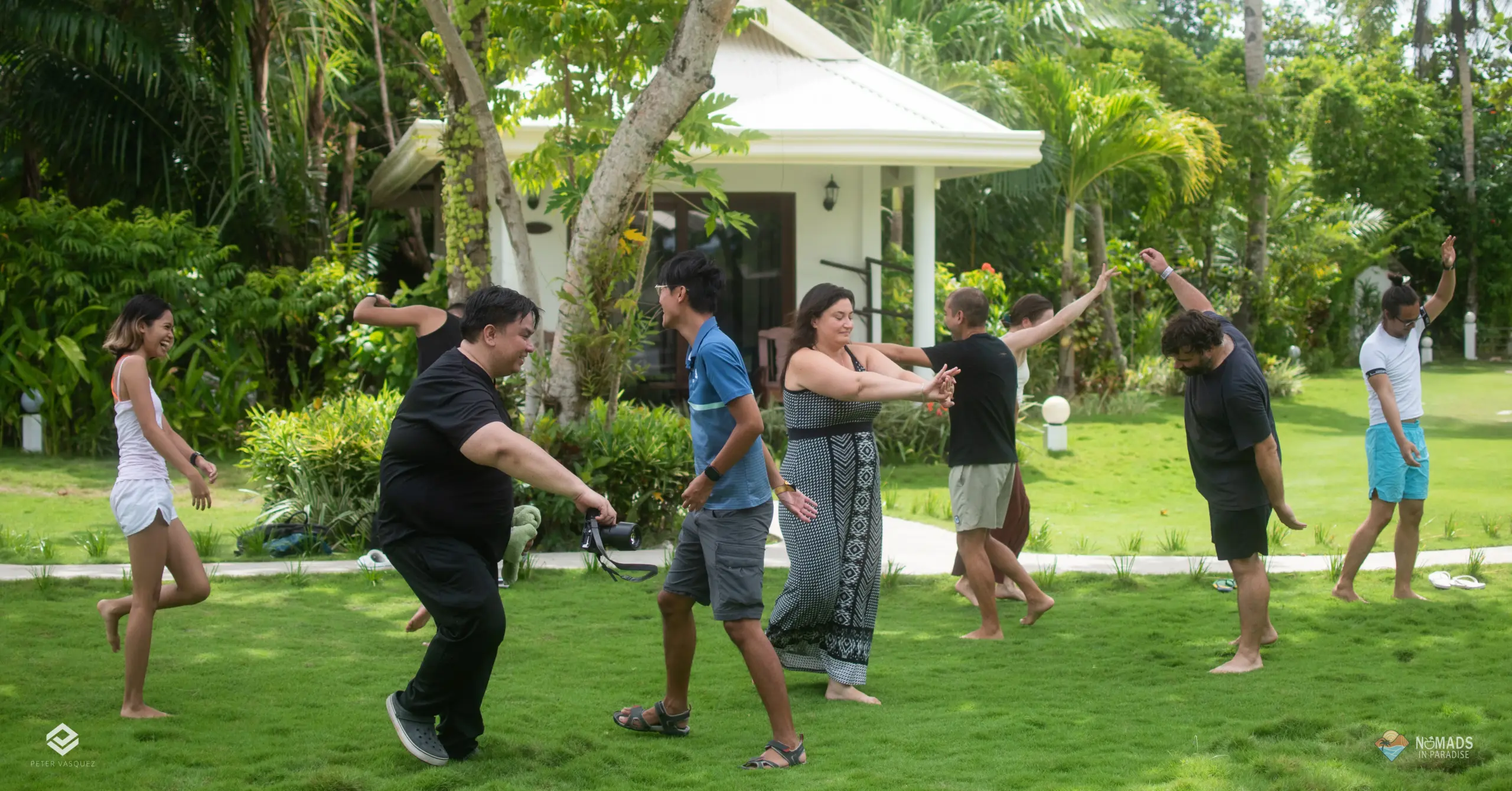 Diverse attendees in playful outdoor movement workshop on lush tropical lawn at Nomads in Paradise