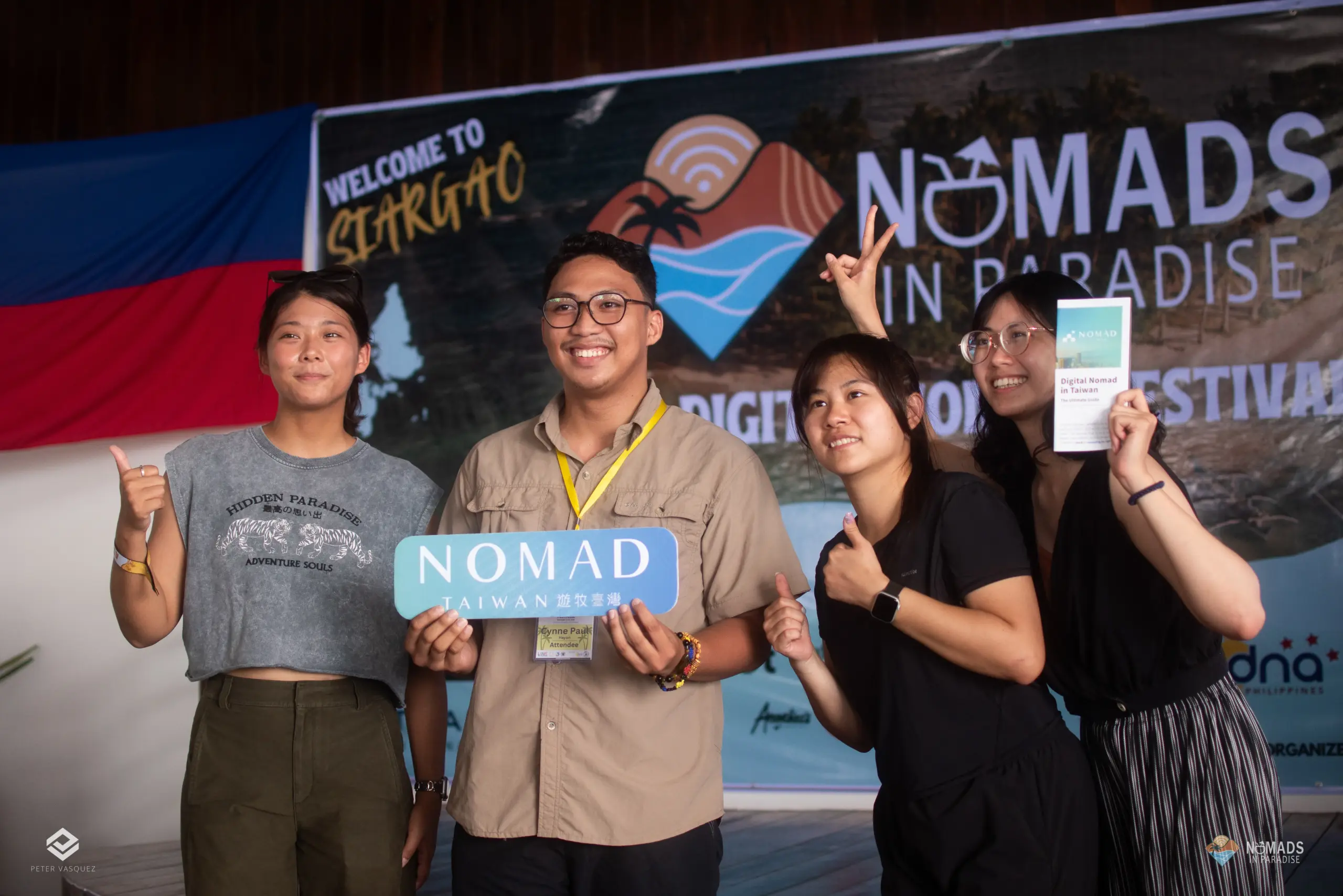 Four smiling attendees holding Nomad Taiwan sign before Welcome to Siargao festival banner