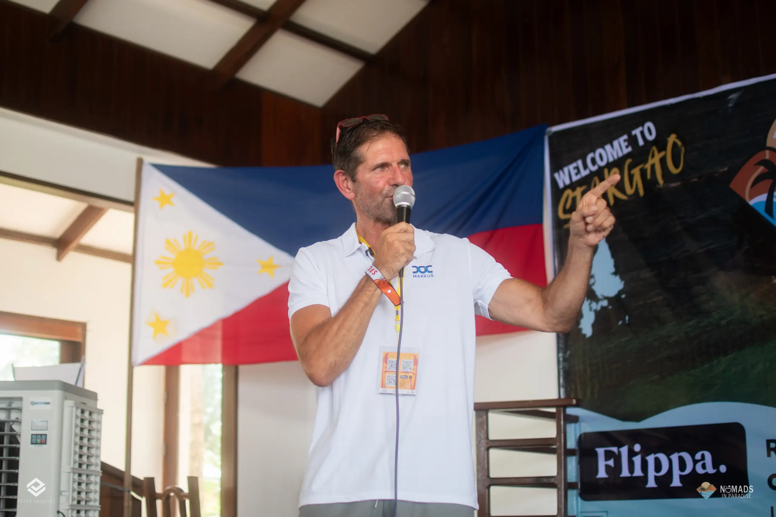 Speaker presenting on stage with Philippine flag and Welcome to Siargao banner — Nomads in Paradise keynote