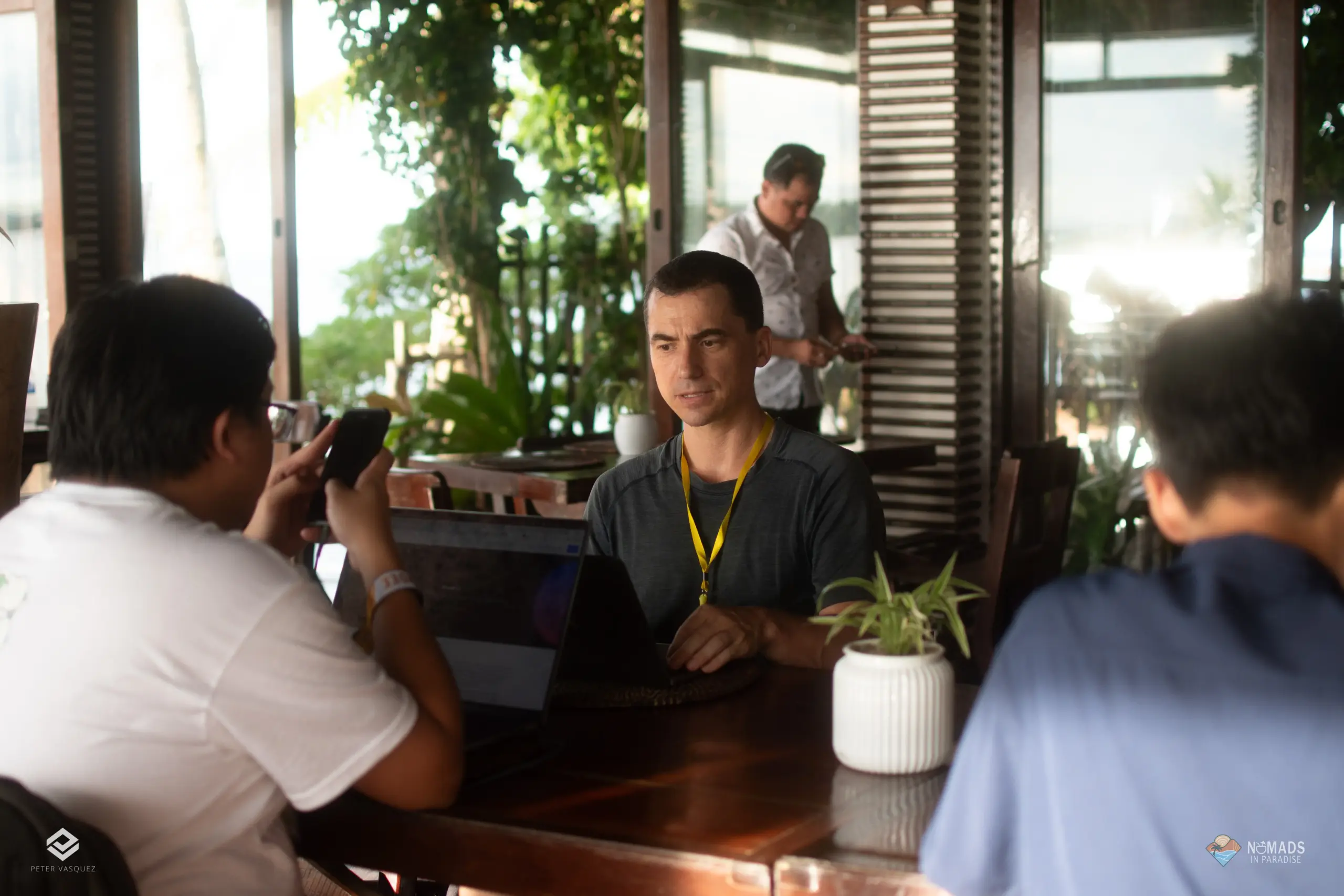 Filipino attendee working on laptop at tropical outdoor cowork table with yellow lanyard