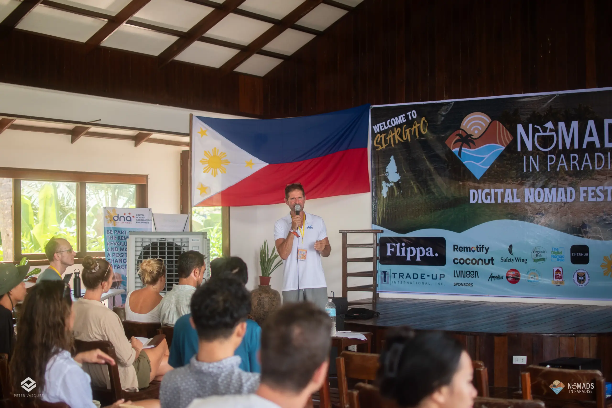 Speaker addressing seated festival audience in bright wooden venue — Nomads in Paradise conference